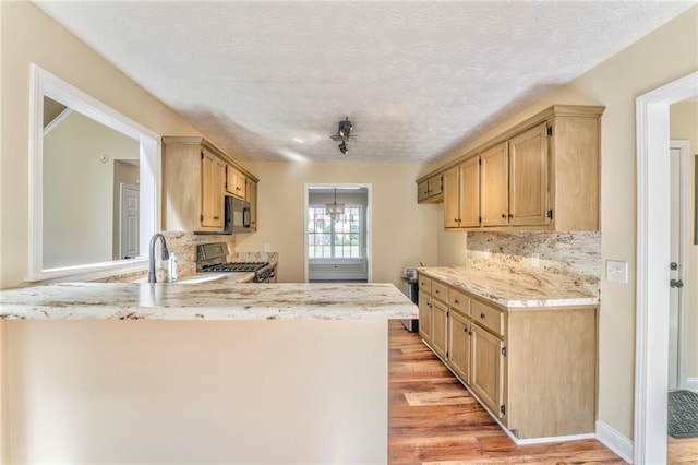 kitchen featuring tasteful backsplash, light hardwood / wood-style flooring, stainless steel stove, sink, and a textured ceiling