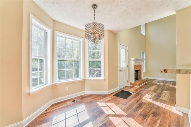 unfurnished dining area with a notable chandelier, a fireplace, wood-type flooring, and a textured ceiling