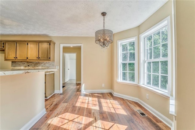 kitchen featuring pendant lighting, an inviting chandelier, light wood-type flooring, and a textured ceiling