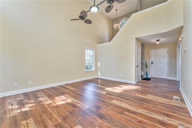 unfurnished living room with ceiling fan with notable chandelier, high vaulted ceiling, and hardwood / wood-style floors