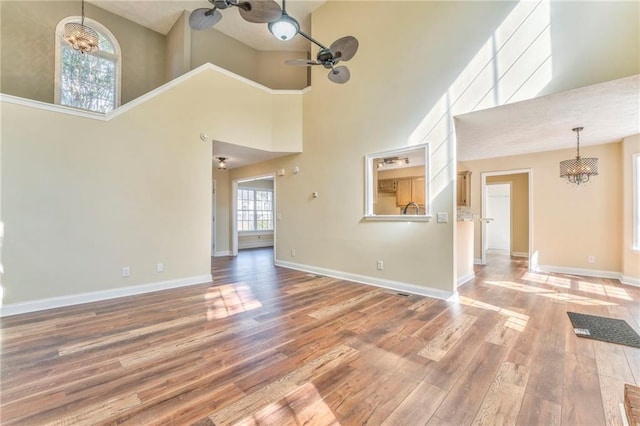 unfurnished living room featuring ceiling fan with notable chandelier, sink, a towering ceiling, and wood-type flooring