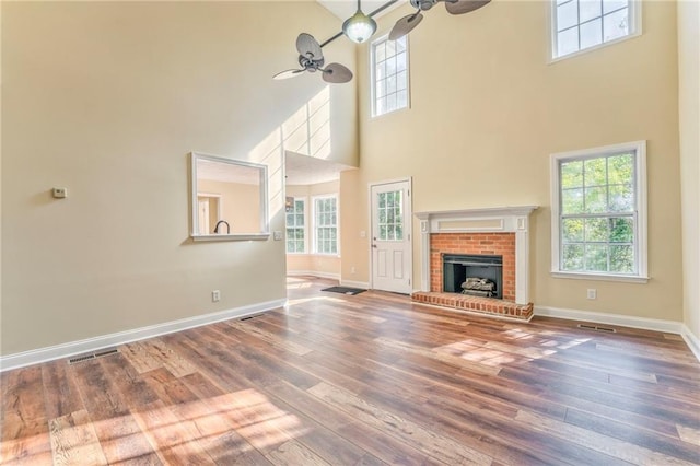 unfurnished living room featuring a high ceiling, a brick fireplace, ceiling fan, and wood-type flooring