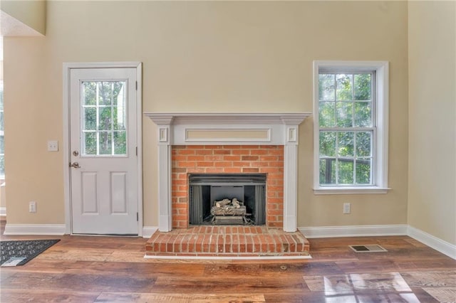 unfurnished living room featuring wood-type flooring, a brick fireplace, and a healthy amount of sunlight