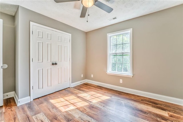 unfurnished bedroom with ceiling fan, a closet, light hardwood / wood-style floors, and a textured ceiling