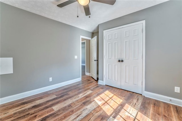 unfurnished bedroom featuring ceiling fan, a textured ceiling, a closet, and wood-type flooring