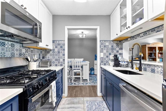 kitchen featuring a textured ceiling, stainless steel appliances, blue cabinets, sink, and white cabinetry