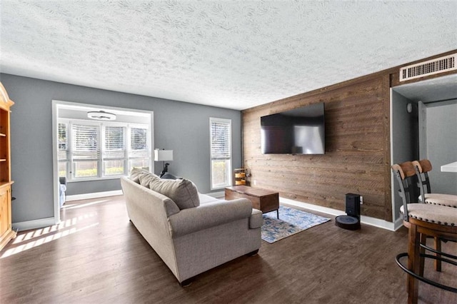 living room featuring a textured ceiling, dark wood-type flooring, and wooden walls