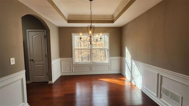 unfurnished dining area with a raised ceiling, crown molding, dark hardwood / wood-style floors, and an inviting chandelier