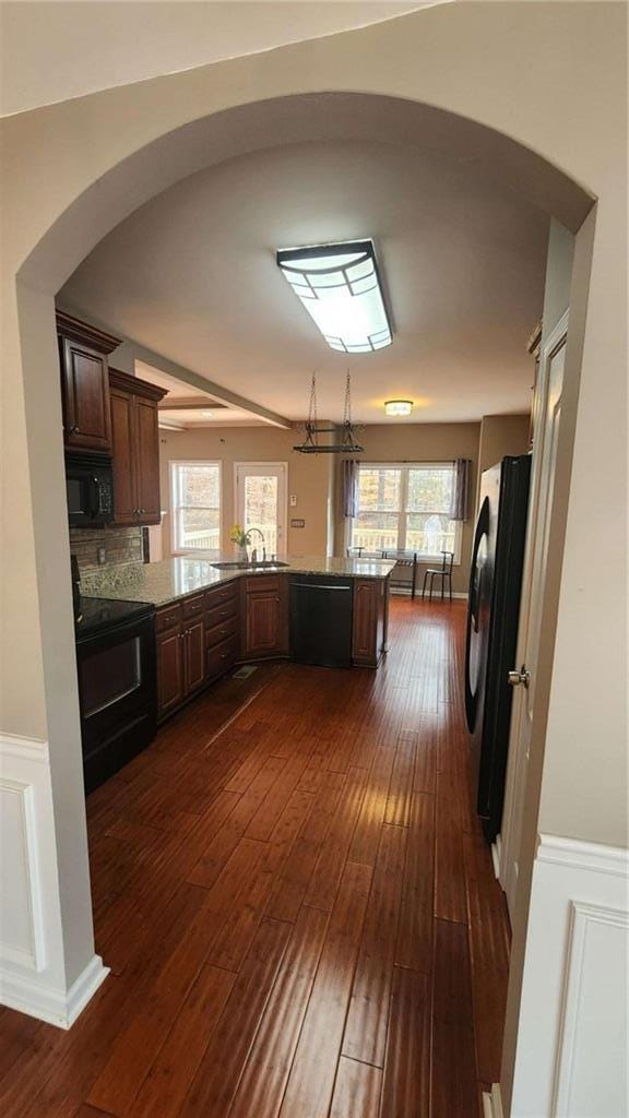 kitchen with dark hardwood / wood-style floors, black appliances, sink, decorative backsplash, and kitchen peninsula