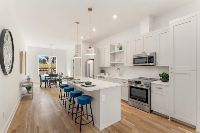 kitchen featuring a center island, white cabinets, light hardwood / wood-style flooring, appliances with stainless steel finishes, and decorative light fixtures