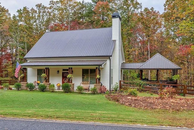 view of front of property with a porch, metal roof, a front yard, and a chimney