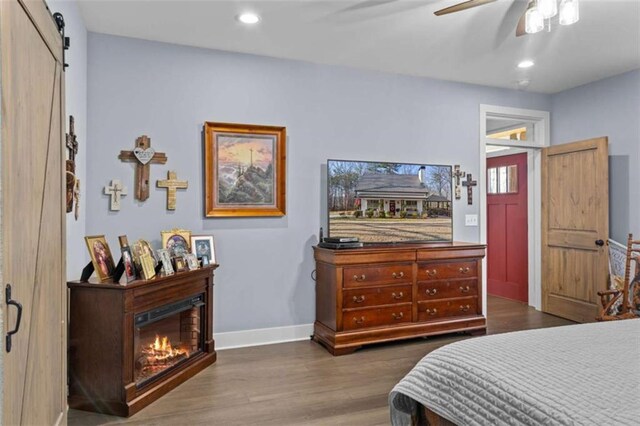 bedroom featuring baseboards, recessed lighting, dark wood-style flooring, a glass covered fireplace, and a barn door