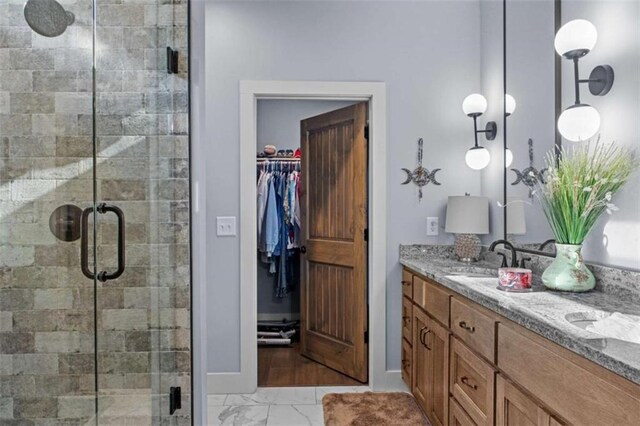 bathroom with double vanity, a stall shower, a sink, a spacious closet, and marble finish floor