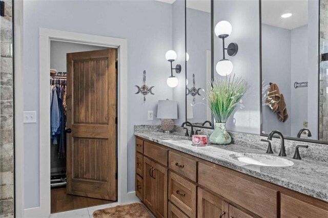 bathroom with a walk in closet, double vanity, tile patterned flooring, and a sink