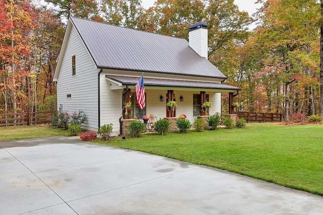 view of front of property with a front lawn, fence, a porch, a chimney, and metal roof