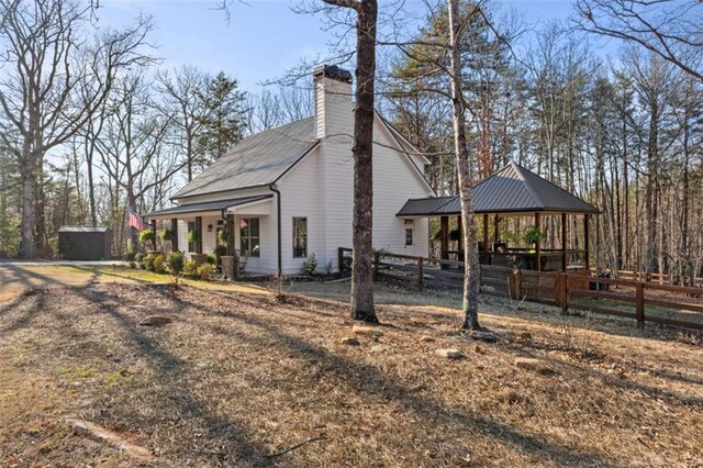 view of property exterior featuring a gazebo, metal roof, a chimney, and fence