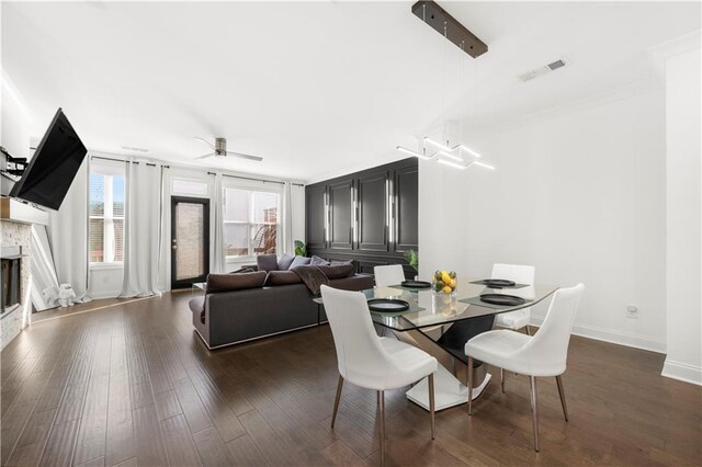 dining space with a stone fireplace, ceiling fan, and dark wood-type flooring