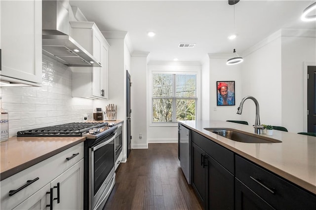 kitchen with sink, wall chimney exhaust hood, stainless steel appliances, pendant lighting, and white cabinets