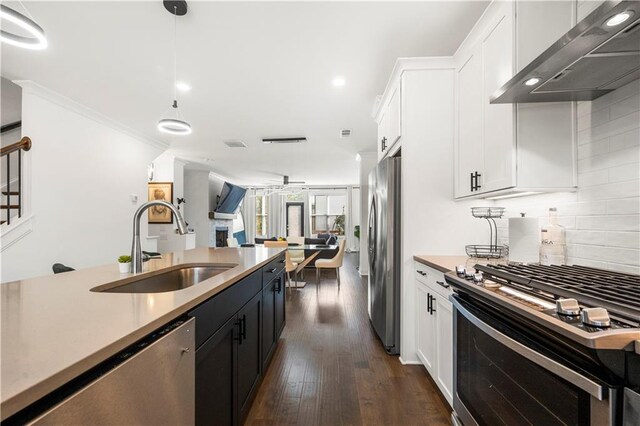 kitchen featuring dark wood-type flooring, white cabinets, hanging light fixtures, wall chimney exhaust hood, and appliances with stainless steel finishes