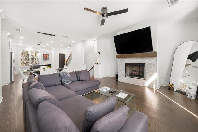 living room with a stone fireplace, ceiling fan, crown molding, and dark hardwood / wood-style floors