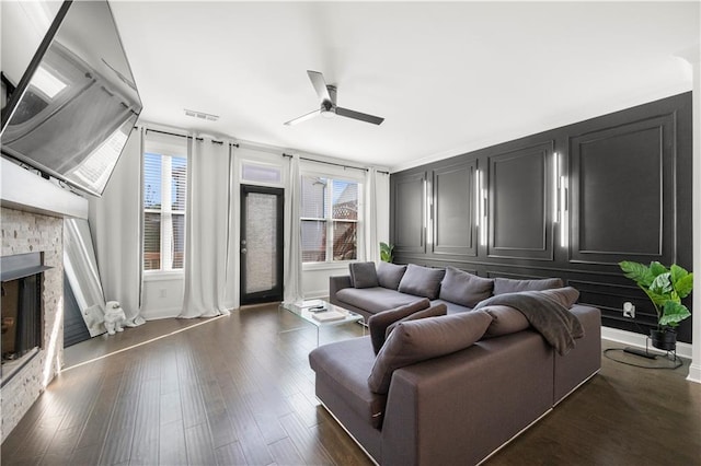 living room featuring dark hardwood / wood-style flooring, a stone fireplace, and ceiling fan