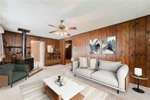 carpeted living room with ceiling fan, a wood stove, and wooden walls