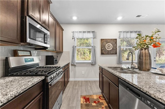 kitchen featuring light stone counters, sink, stainless steel appliances, and light hardwood / wood-style floors