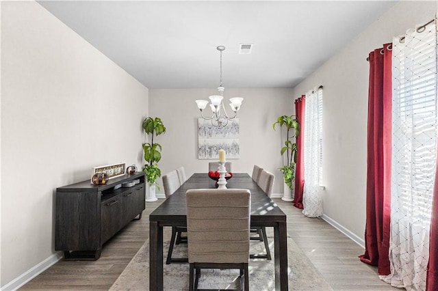 dining space with a healthy amount of sunlight, light wood-type flooring, and an inviting chandelier