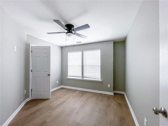 spare room with a ceiling fan, visible vents, baseboards, and wood finished floors