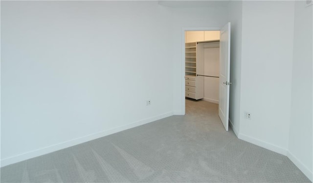 unfurnished bedroom featuring light colored carpet, a walk in closet, a closet, and baseboards