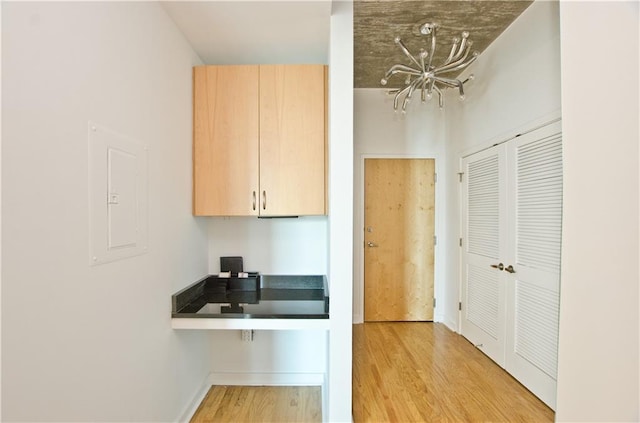 kitchen featuring light wood-type flooring, electric panel, light brown cabinets, and baseboards