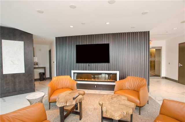 living area featuring marble look tile flooring, an accent wall, recessed lighting, baseboards, and a glass covered fireplace