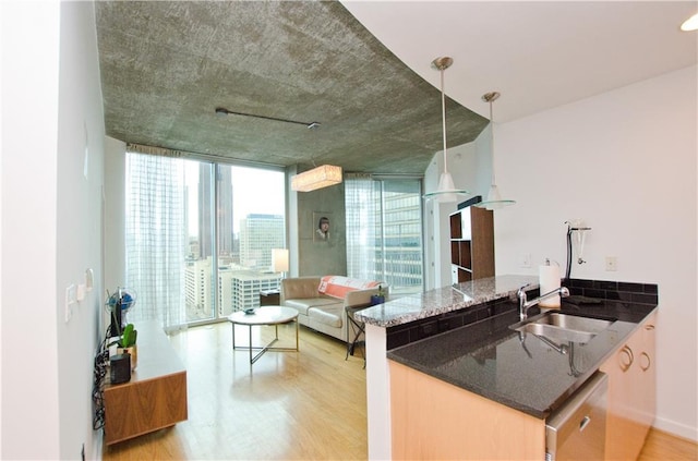 kitchen with a sink, light wood-style floors, dark stone countertops, expansive windows, and a peninsula