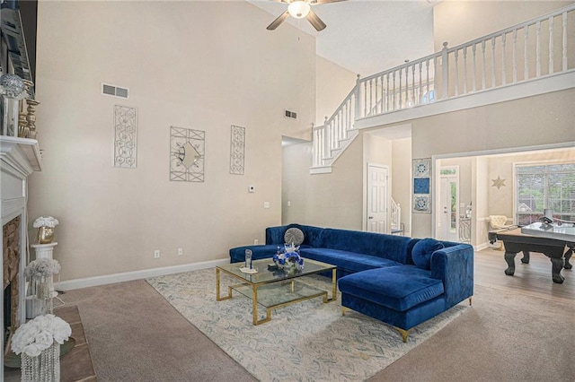 living area featuring carpet floors, ceiling fan, a fireplace with raised hearth, visible vents, and a towering ceiling