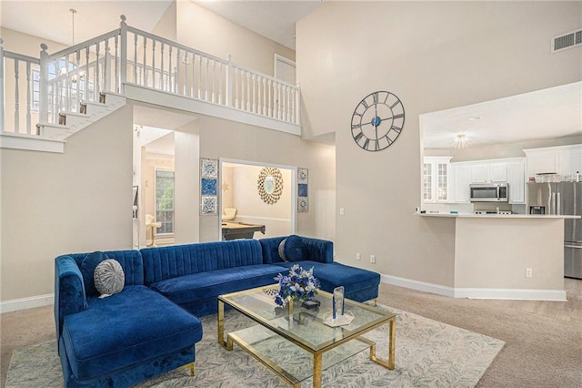 carpeted living area with baseboards, visible vents, a healthy amount of sunlight, and a towering ceiling