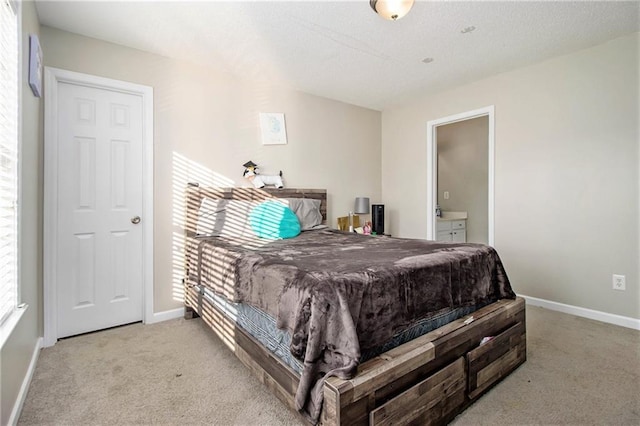 carpeted bedroom with ensuite bathroom, a textured ceiling, and baseboards