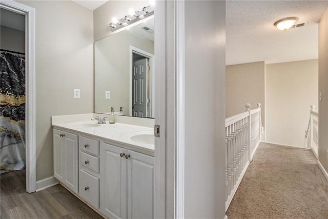 full bath with a sink, double vanity, visible vents, baseboards, and wood finished floors