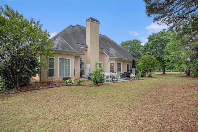 back of property with a patio, a chimney, roof with shingles, stucco siding, and a yard