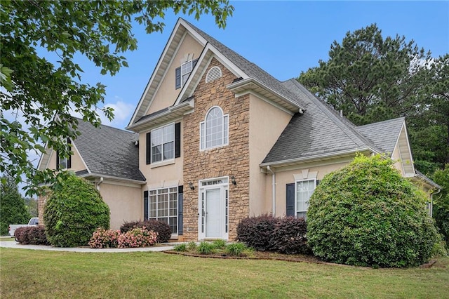 view of front facade featuring a front yard, stone siding, stucco siding, and a shingled roof