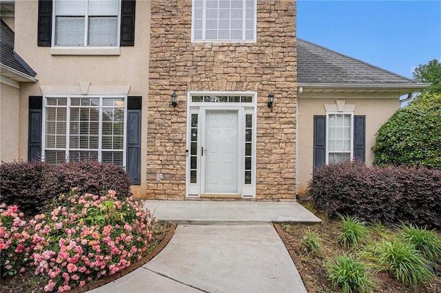property entrance featuring stucco siding, roof with shingles, and stone siding
