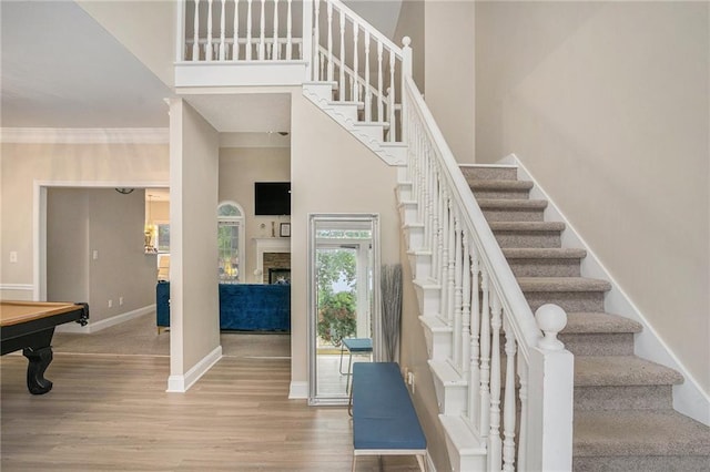 stairs with a fireplace, a towering ceiling, wood finished floors, and baseboards