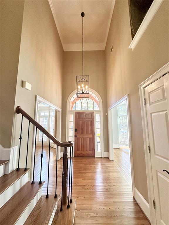 foyer entrance with a high ceiling, a chandelier, light hardwood / wood-style flooring, and crown molding