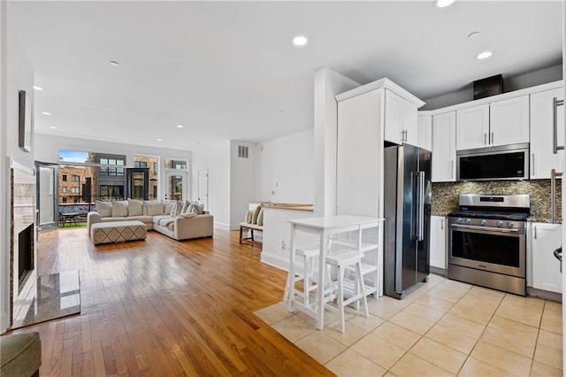 kitchen featuring tasteful backsplash, appliances with stainless steel finishes, light wood-type flooring, and white cabinets