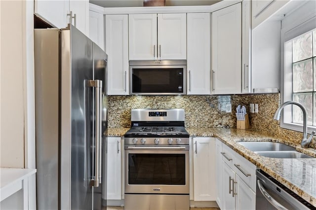 kitchen with light stone counters, appliances with stainless steel finishes, sink, and white cabinets