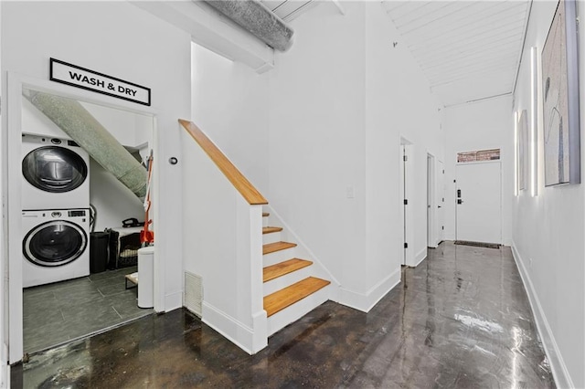 stairs with stacked washer and dryer, a towering ceiling, and concrete flooring