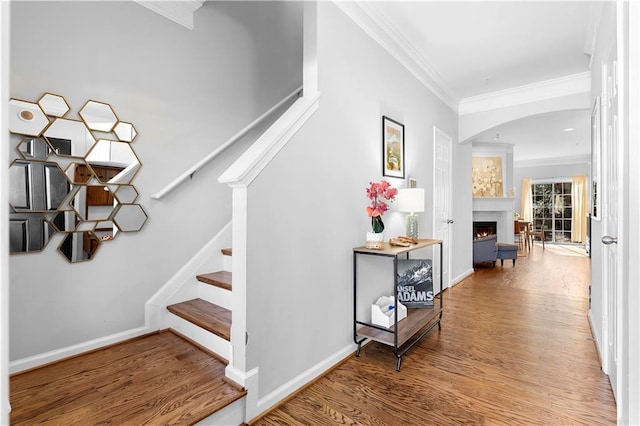 stairway with wood-type flooring, a fireplace, and crown molding