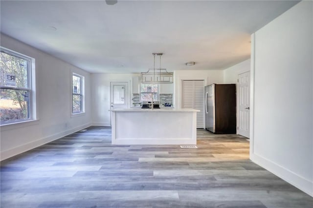 kitchen with stainless steel refrigerator, light hardwood / wood-style flooring, a kitchen island, and pendant lighting