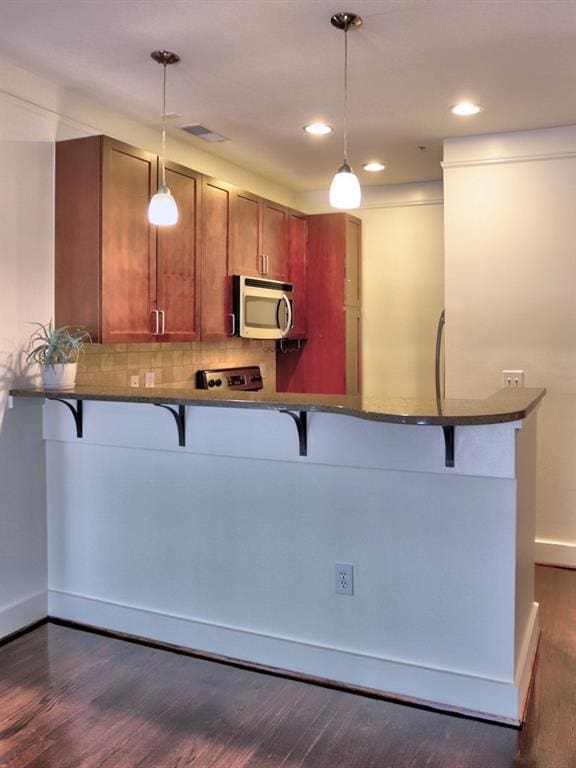 kitchen featuring dark hardwood / wood-style floors, a kitchen bar, kitchen peninsula, and hanging light fixtures