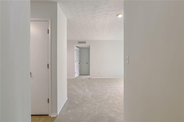 hallway featuring light carpet and a textured ceiling