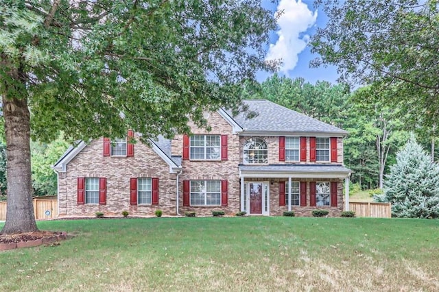 colonial home with a shingled roof, fence, and a front lawn